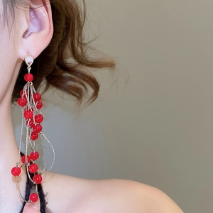 Detail of elegant long tassel earrings with vibrant red beads and gold chain on model