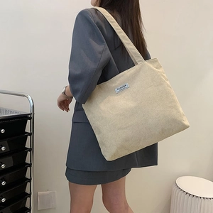 Detail of beige corduroy tote bag showing soft ribbed texture and fashion label on shoulder