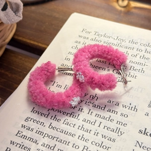 Macro shot of pink flocked C-shaped hoop earrings with silver snowflake accents on a book