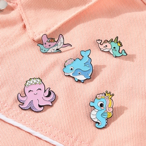 Detail of five ocean animal enamel pins including octopus and seahorse on pink corduroy fabric