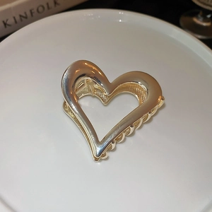 Close-up of golden hollow heart hair claw clip on white ceramic plate background