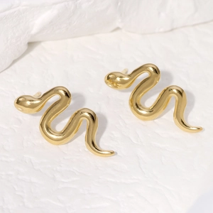 Macro view of gold snake-shaped stainless steel stud earrings on a textured surface
