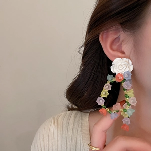 Close-up of sweet acrylic colorful flower drop earrings worn by a model on a beige background