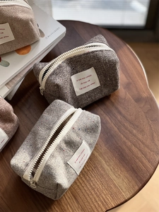 Detail of tweed herringbone makeup bags in grey and brown on a wooden table with books