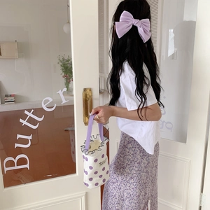 Lifestyle view of a purple polka dot canvas mini handbag held by a woman in a floral skirt