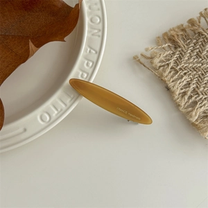 Macro detail of amber resin hair clip with France Handmade logo on a vintage tray