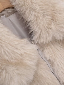 Gros plan sur la texture de fausse fourrure blanc cassé et le détail du zip en métal argenté