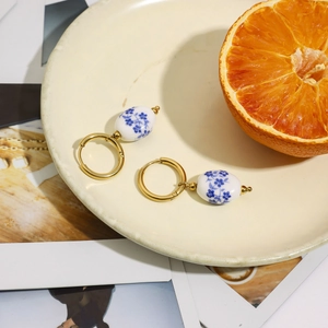 Dettaglio di orecchini a cerchio in acciaio dorato 18K con ciondoli in ceramica blu e bianca