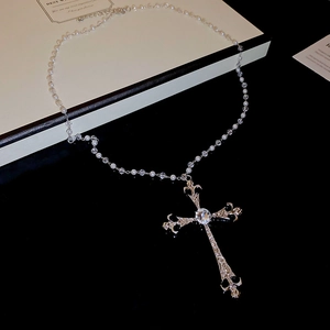 Dettaglio del ciondolo a croce vintage con incisioni barocche e collana di perle finte