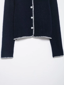 Detailed macro view of navy knit cardigan with scalloped light gray crochet trim and buttons