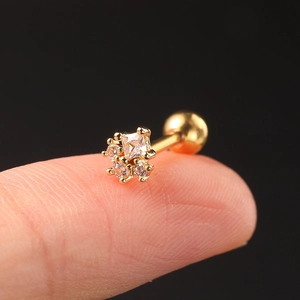 Macro view of a tiny gold geometric stud earring with zircons held on a fingertip