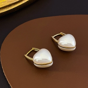 Détail macro de boucles d'oreilles en perle en forme de cœur dorées sur cuir brun