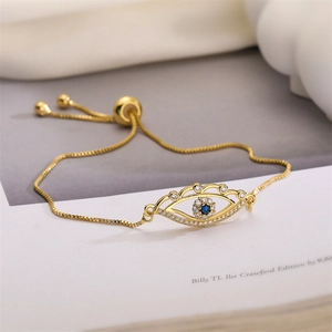 Close-up of golden box chain bracelet featuring a cubic zirconia evil eye charm and slide clasp