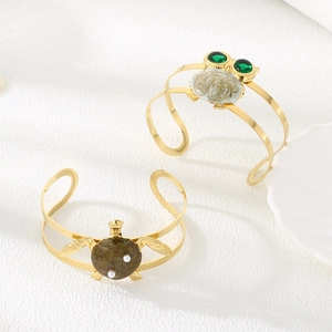 Detail view of gold owl and turtle bangles with green gemstones and white pearls