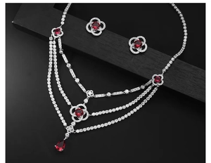 Macro detail of silver necklace and red gemstone earrings set against black background