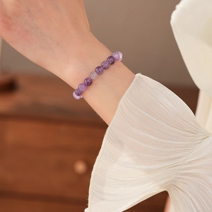 Nahaufnahme eines Amethyst-Perlenarmbands am Handgelenk mit elegantem Stoffhintergrund