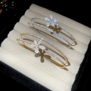 Detailed view of silver and gold zircon flower bangles on velvet display with sparkle effects