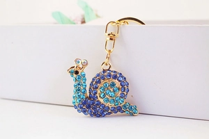 Macro shot of snail keychain featuring gradient blue rhinestones on a golden metal shell
