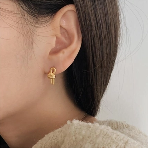 Close-up of a model wearing minimalist gold-tone knot stud earring in a warm, daily setting