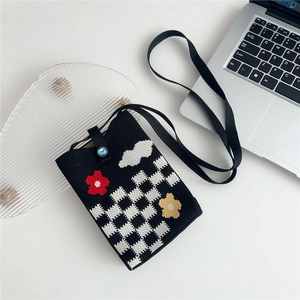 Detail of knitted phone bag with checkered pattern, floral jacquard and blue jewel button