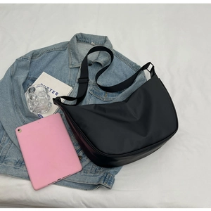 Flat lay of a black nylon crossbody bag on a denim jacket with lifestyle accessories