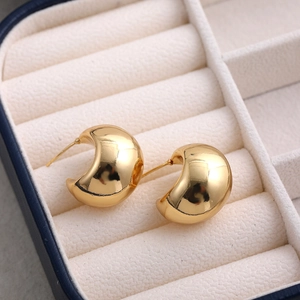 Close-up of polished 18K gold hollow geometric C-shaped stud earrings in a jewelry box