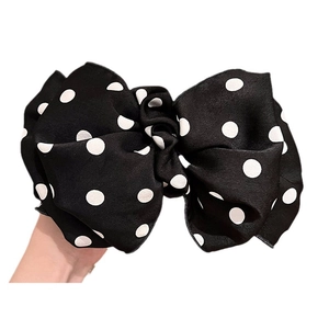 Black polka dot bow hair clip with layered 3D design and white dots held in hand