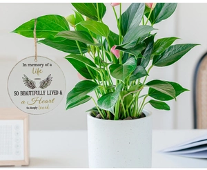 Close-up of a round wooden Christmas ornament with angel wings and memorial quote on a plant