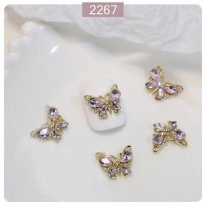 Macro detail of 3D crystal butterfly nail charms with pink stones and gold alloy base