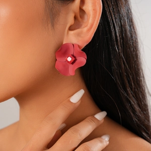 Detail of red floral stud earring with a square red gemstone on a model's ear