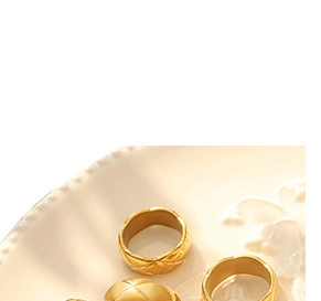 Macro shot of gold-plated geometric rings with quilted pattern on a white ceramic plate