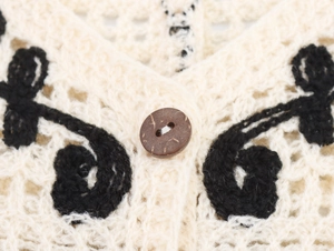 Detail of crochet floral knit vest with cream hollow pattern and natural wooden button