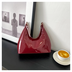 Detail of glossy burgundy patent leather hobo bag with gold hardware on a table
