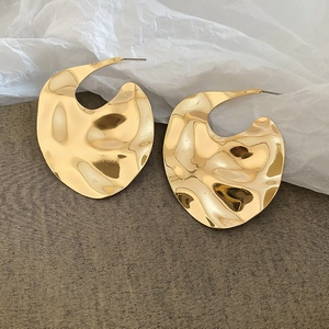 Detail view of irregular hammered gold C-shaped earrings with molten lava texture finish