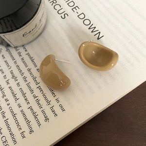 Detailed view of khaki resin C-shaped bean stud earrings resting on a vintage book