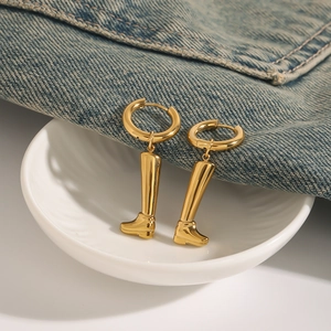 Detailansicht der 18k vergoldeten Ohrhänger in Stiefelform auf blauem Denim und Keramik