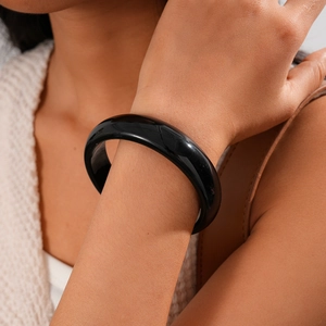 Close-up of minimalist wide black resin bangle bracelet on model with warm knitwear background