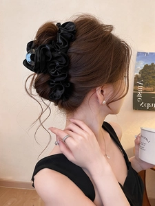 Détail d'une grande pince à cheveux en tissu plissé noir sur un chignon élégant