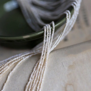 Micro-shot of tiny white freshwater pearls draped over a vintage dark green ceramic bowl