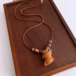 Close-up of plush puppy pendant with wooden beads and red accents on brown cord