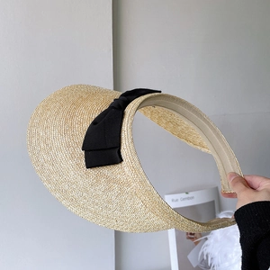 Detail of hand-woven beige straw visor with a black grosgrain ribbon bow decoration