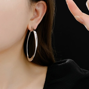 Close-up of a model wearing large silver chunky twist hoop earrings on a black background