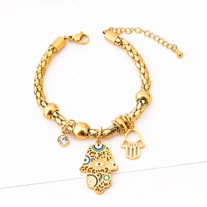 Gold beaded bracelet with Hamsa Hand and Evil Eye charms on white textured background