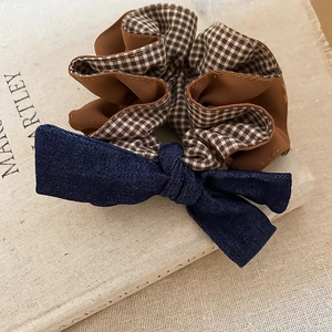 Detail of blue denim bow and brown plaid fabric scrunchie on a textured background