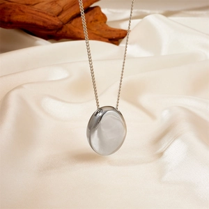 Macro shot of polished silver pebble pendant on smooth silk fabric background