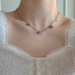 Elegant gold necklace with purple flower pendants and beads on a model wearing white lace