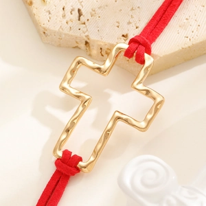 Detail of a golden cross pendant with hammered texture and red braided ropes