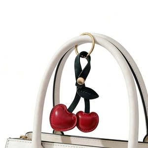 Detail of red leather cherry keychain with green leaves on white handbag handle