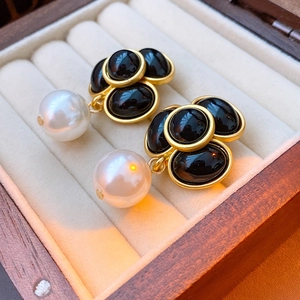 Macro shot of gold heart earrings with black gems and pearls on a wooden jewelry box