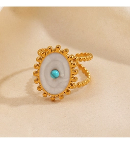 Détail d'une bague dorée avec résine ovale blanche et incrustation de perle turquoise